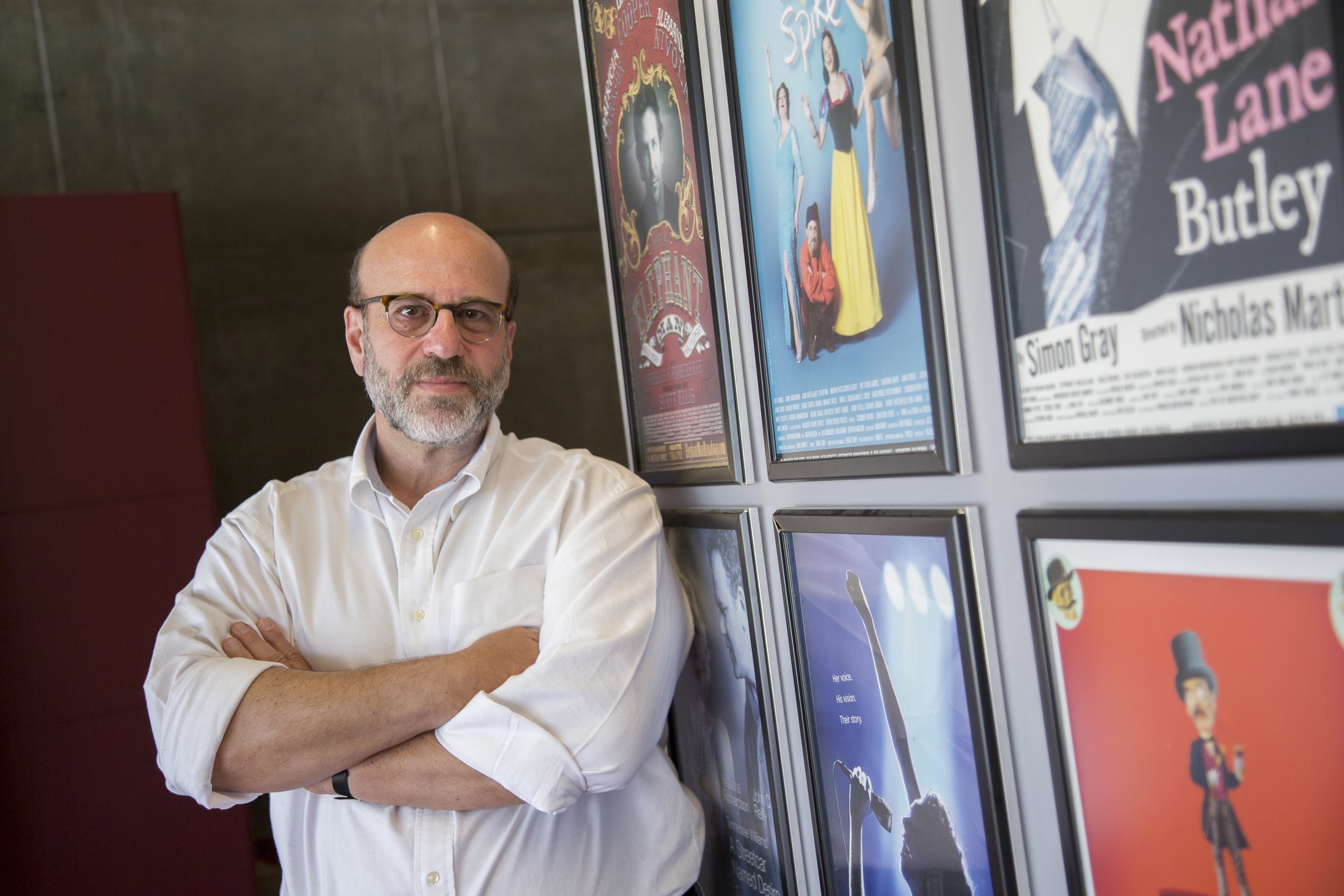 Larry Hirschhorn, arms crossed, beside a wall of framed Broadway posters